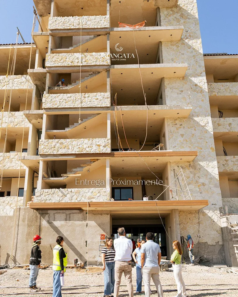 Grupo de personas frente a la fachada en obra de Mangata, con el rotulo «Entrega proximamente»