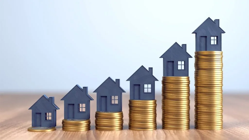 Monedas apiladas en ascenso, con casas encima, como representacion de la plusvalia