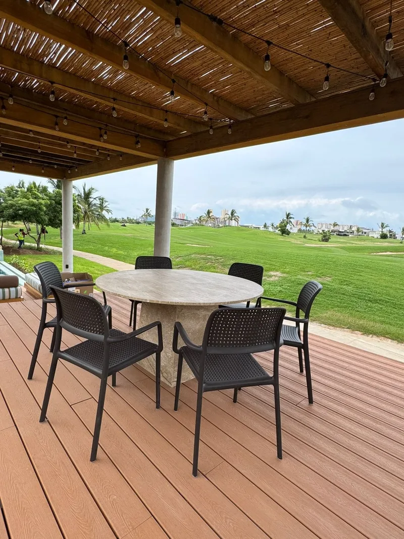 Comedor exterior bajo pergola de madera, con vista al campo de golf