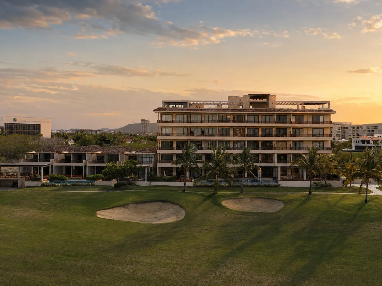 Edificio de departamentos de Mangata Golf & Living al atardecer, visto desde el campo de golf con dos búnkeres de arena en primer plano